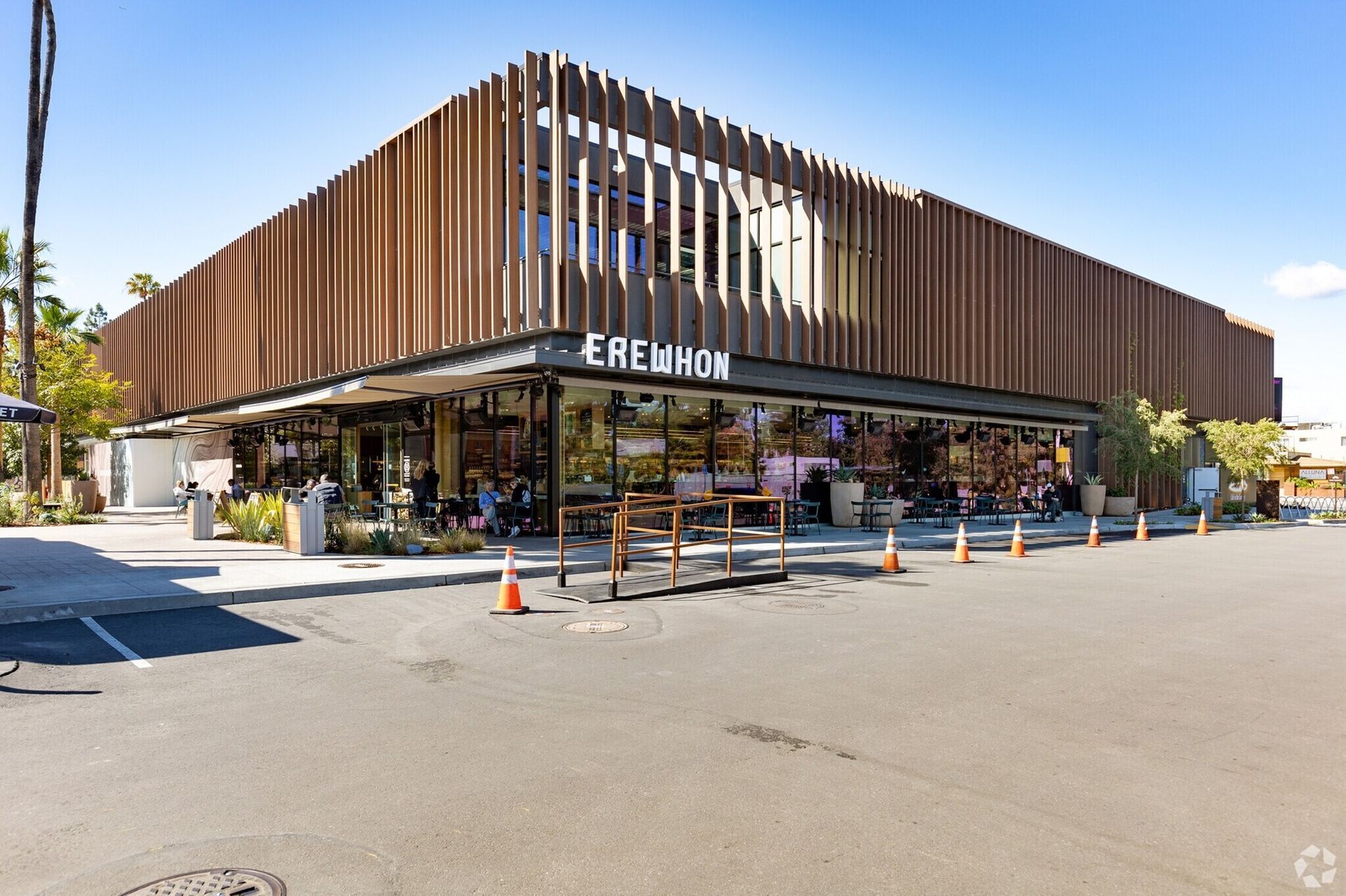 An Erewhon organic grocery store with a modern, vertical wood-slat facade in a sunny parking lot.