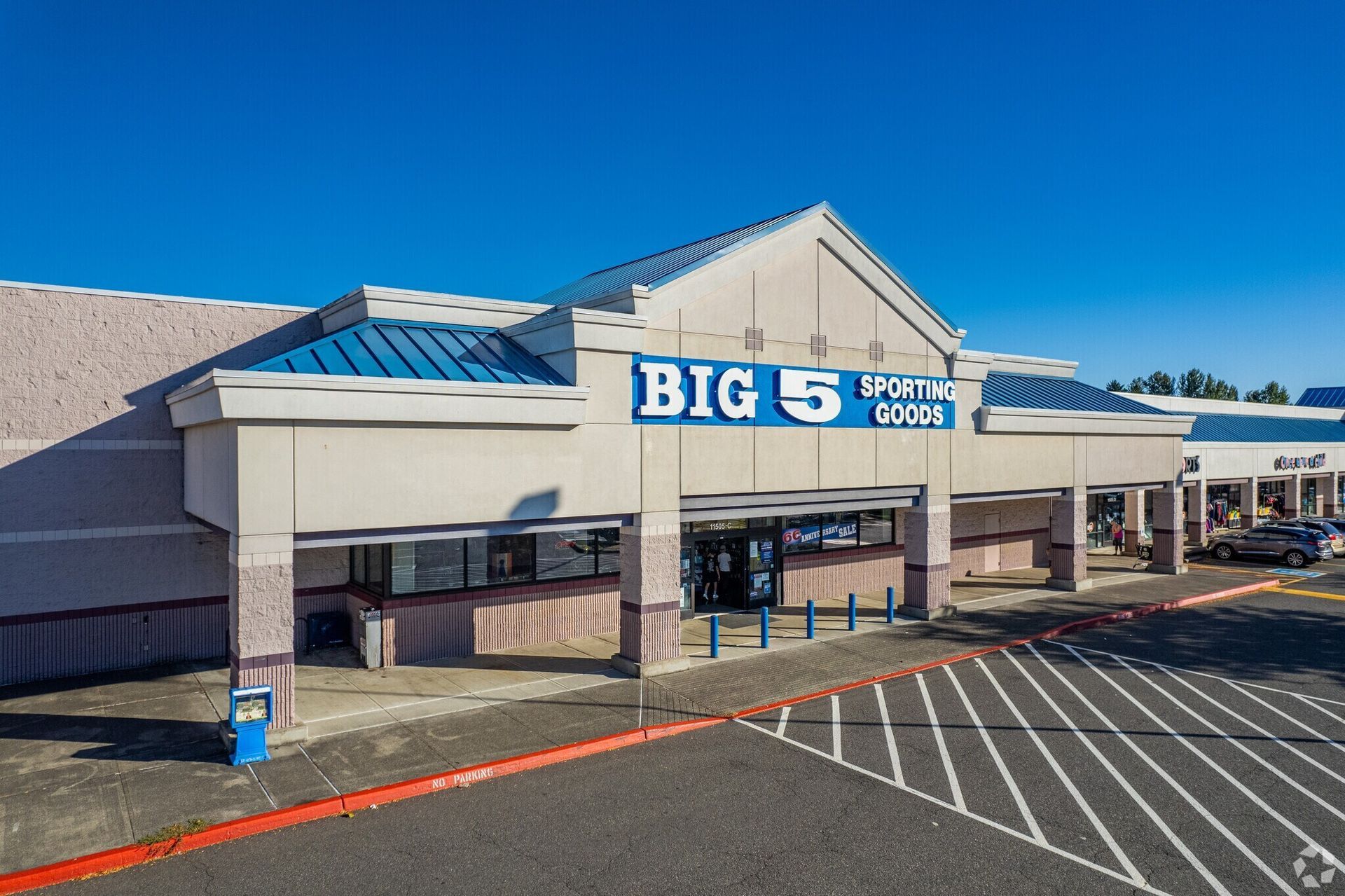 Exterior view of a Big 5 Sporting Goods store in a strip mall under a clear blue sky.