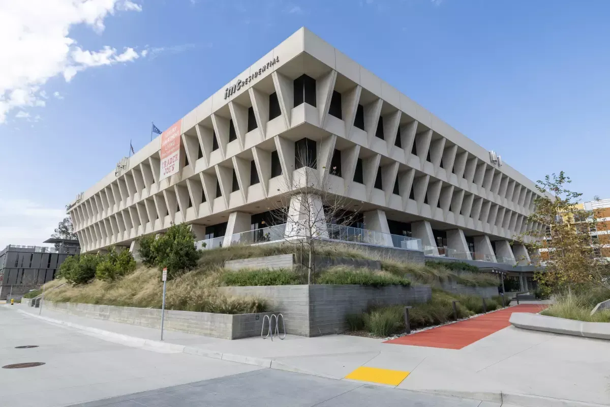 Modern, Brutalist-style office building with an angular concrete facade on a landscaped corner lot under a blue sky.