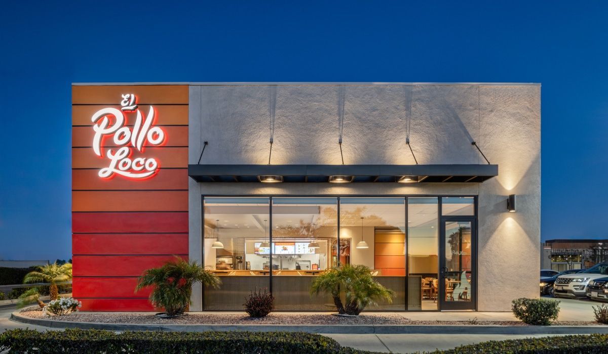 El Pollo Loco restaurant exterior at dusk, featuring a red and orange striped accent wall and floor-to-ceiling windows.