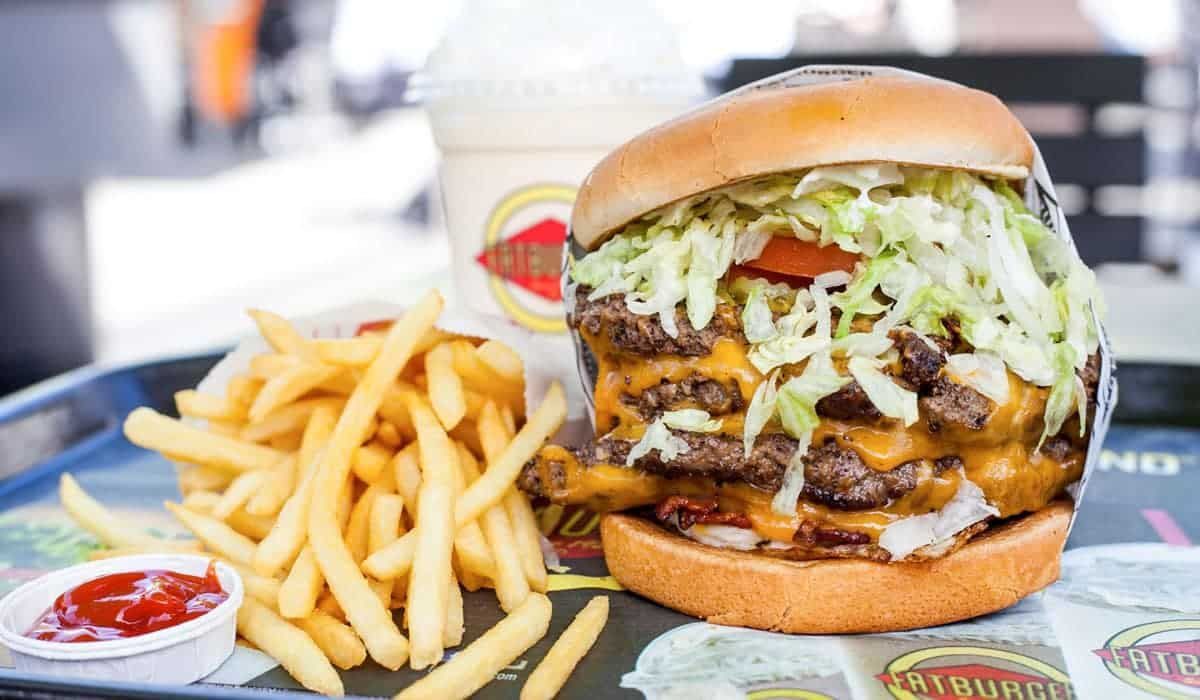 A tray holding a large double cheeseburger piled with lettuce, a side of french fries, ketchup, and a milkshake.