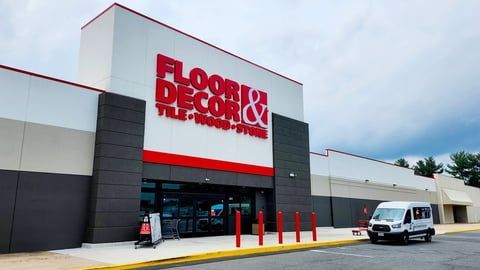 A Floor & Decor store exterior featuring white and gray walls with red signage and a white van parked in front.