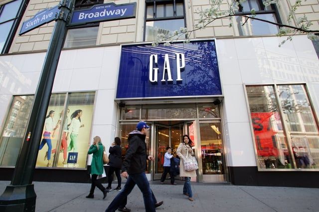 People walk past a Gap store located at the corner of Sixth Avenue and Broadway on a sunny day.