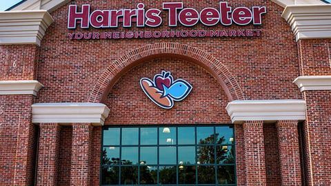 Harris Teeter store front exterior with red brick walls, large glass windows, and a logo featuring bread, an apple, and fish.