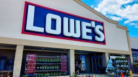 The exterior of a Lowe’s home improvement store with its large blue and red logo, under a blue sky with white clouds.