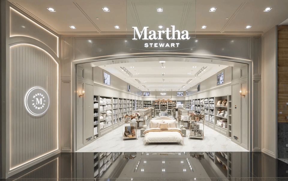 Elegant Martha Stewart home goods store interior with neutral-toned bedding and decor displays.