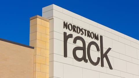 The Nordstrom Rack logo sign on the exterior of a tan building against a bright blue sky.