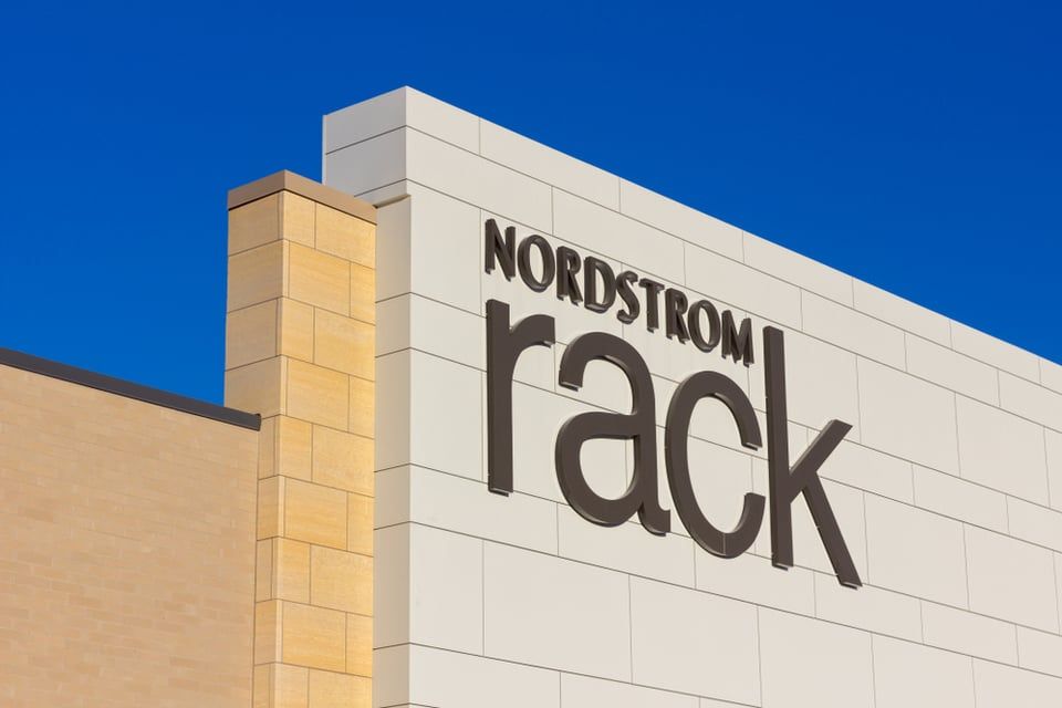 The exterior sign for a Nordstrom Rack store with tan block walls against a clear blue sky.