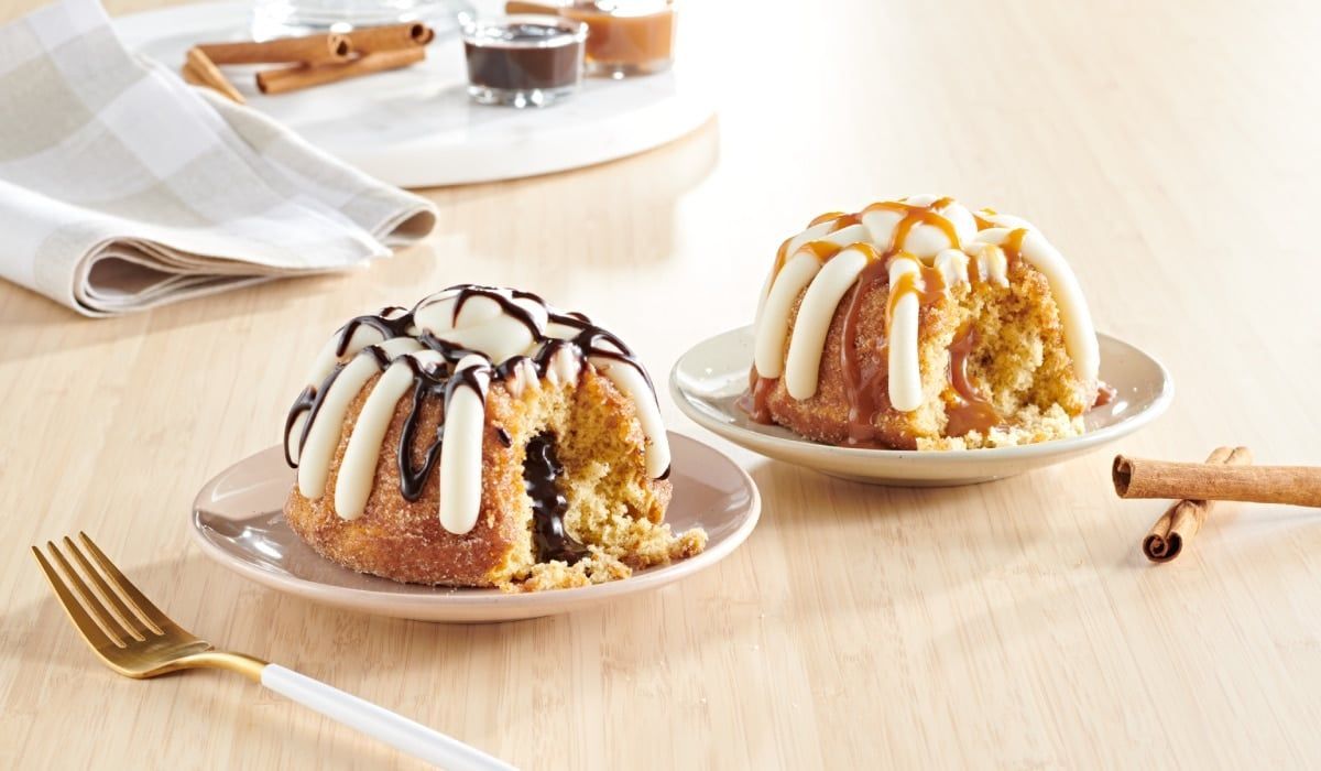 Two bundt cakes on small plates: one with chocolate drizzle, one with caramel drizzle, with cinnamon sticks nearby.