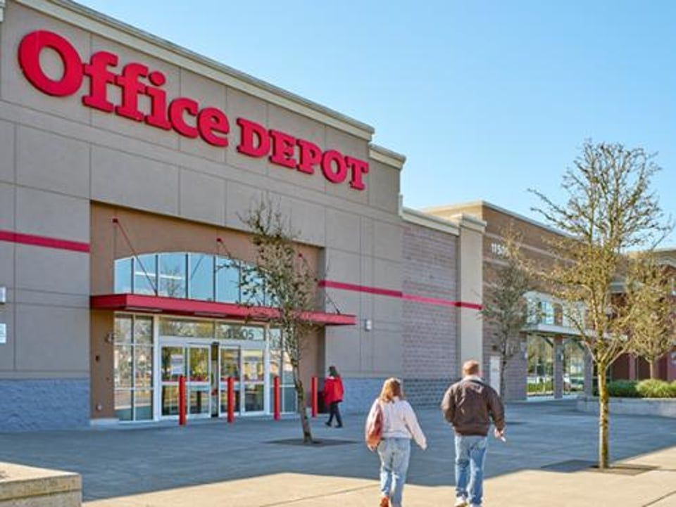 People walking toward the entrance of an Office Depot store on a sunny day.