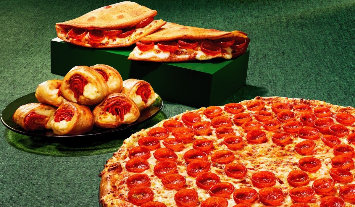 A pepperoni pizza is sitting on a table next to a plate of pastries.