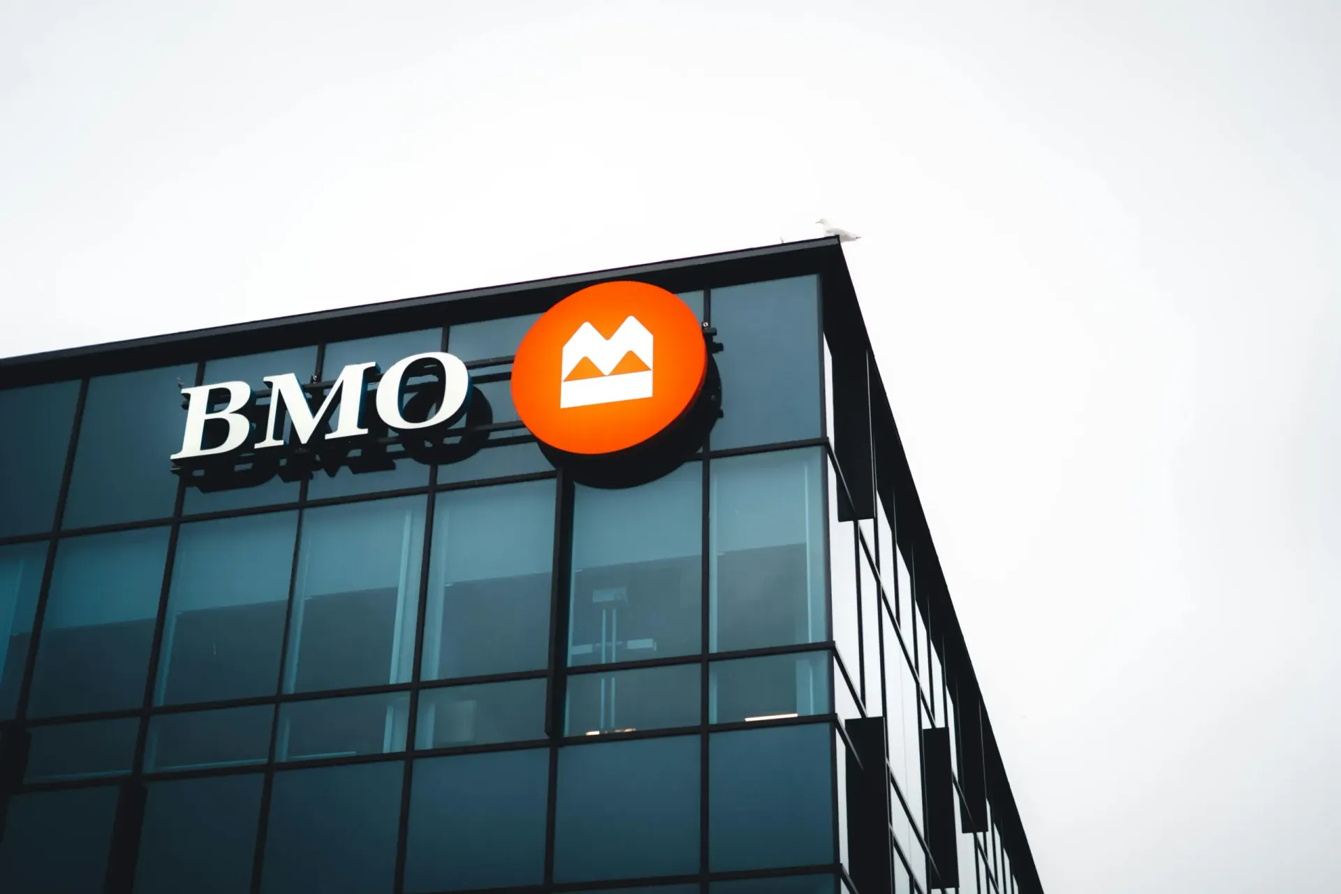 The exterior of a modern glass building with a BMO sign and a circular orange logo featuring a stylized white letter M.