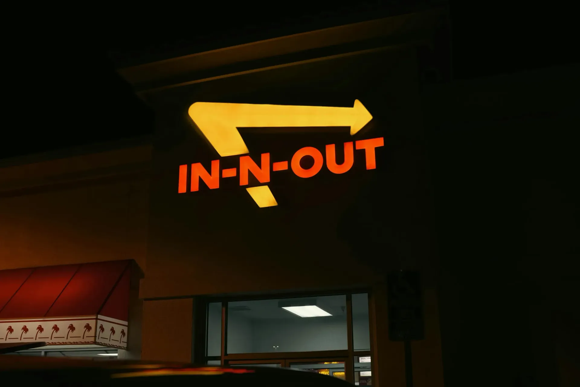 An In-N-Out Burger sign glowing yellow and red on a building exterior at night.