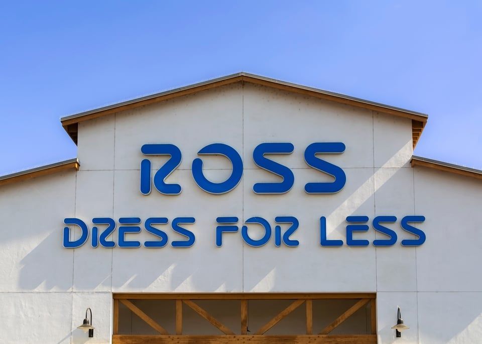 A blue Ross Dress for Less sign mounted on the white facade of a building against a clear blue sky.