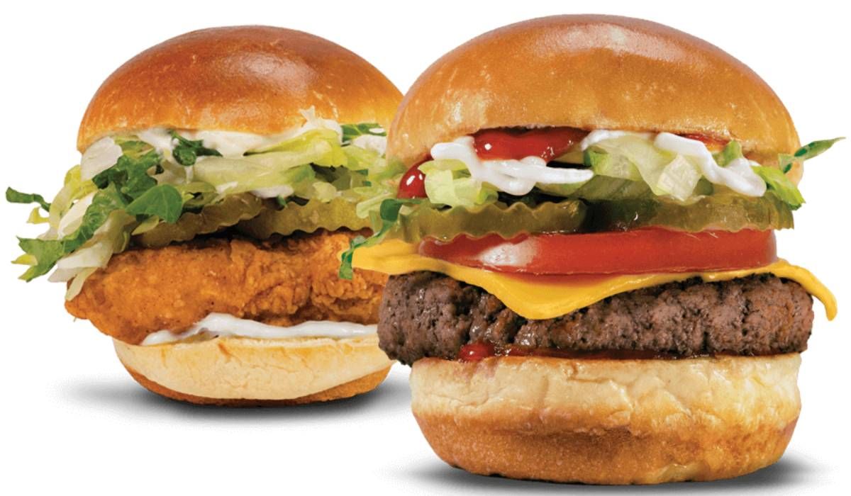 A side-by-side view of a crispy chicken sandwich and a cheeseburger with tomato, lettuce, and pickles on a white background.