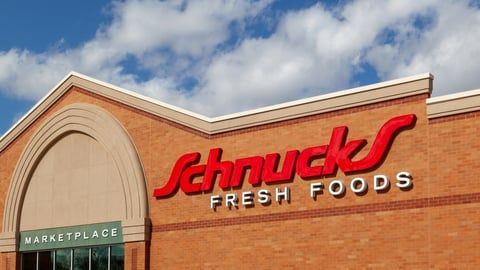 A red Schnucks Fresh Foods sign on a brick building exterior under a blue sky with white clouds.