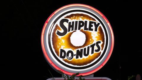 A glowing, circular sign for Shipley Do-Nuts featuring the brand name over a donut graphic against a dark background.