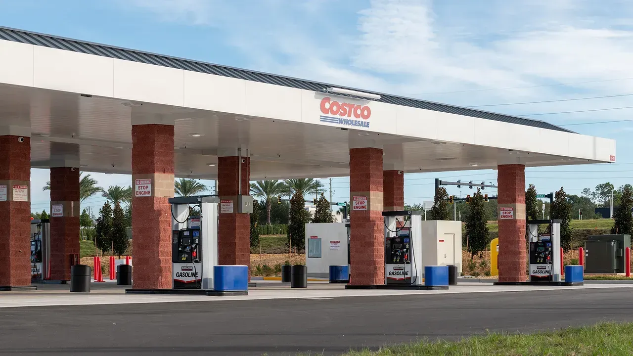 A modern, empty Costco gas station with a large white canopy supported by brick pillars on a sunny day.