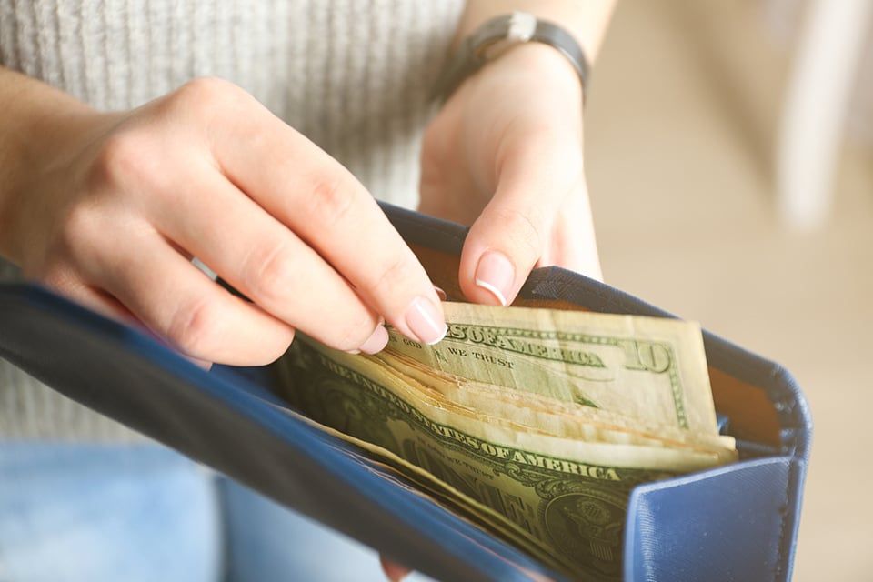 A person holding an open blue wallet containing several US dollar bills.