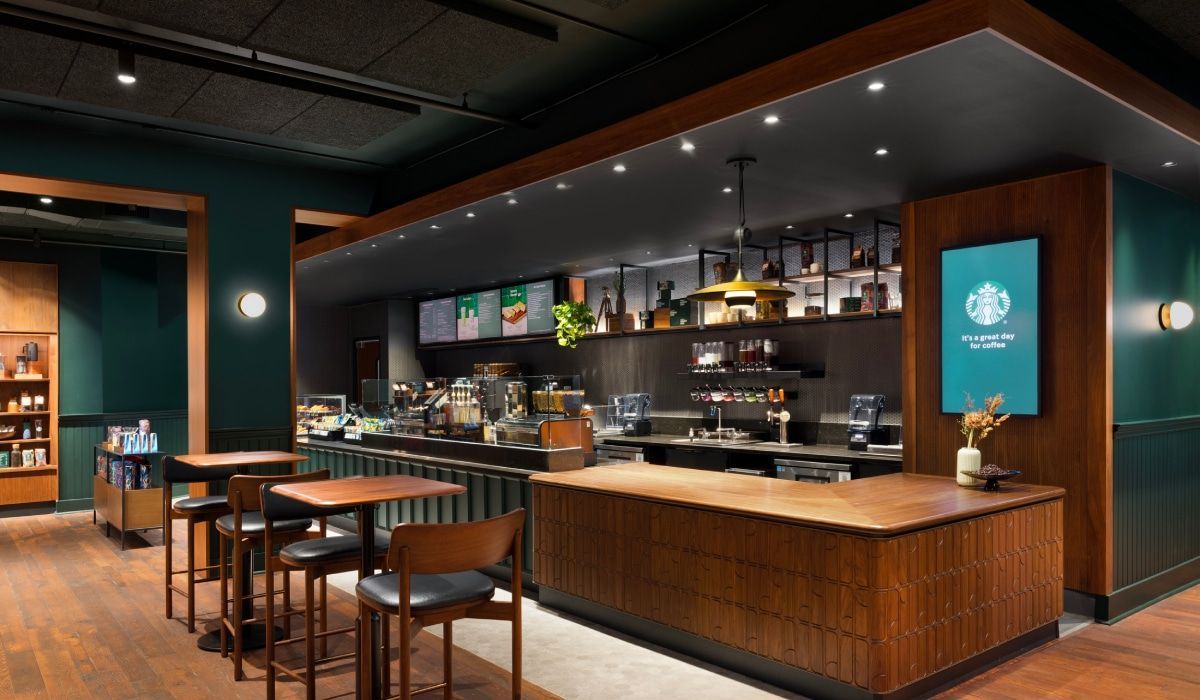 Modern Starbucks cafe interior featuring a wooden counter, dark green walls, pendant lighting, and café-style seating.