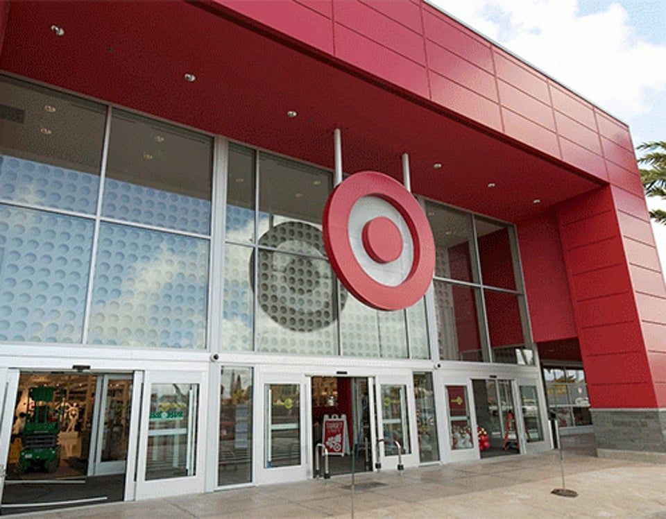 A Target store entrance with red paneled walls, floor-to-ceiling glass windows, and a large red target logo hanging above.