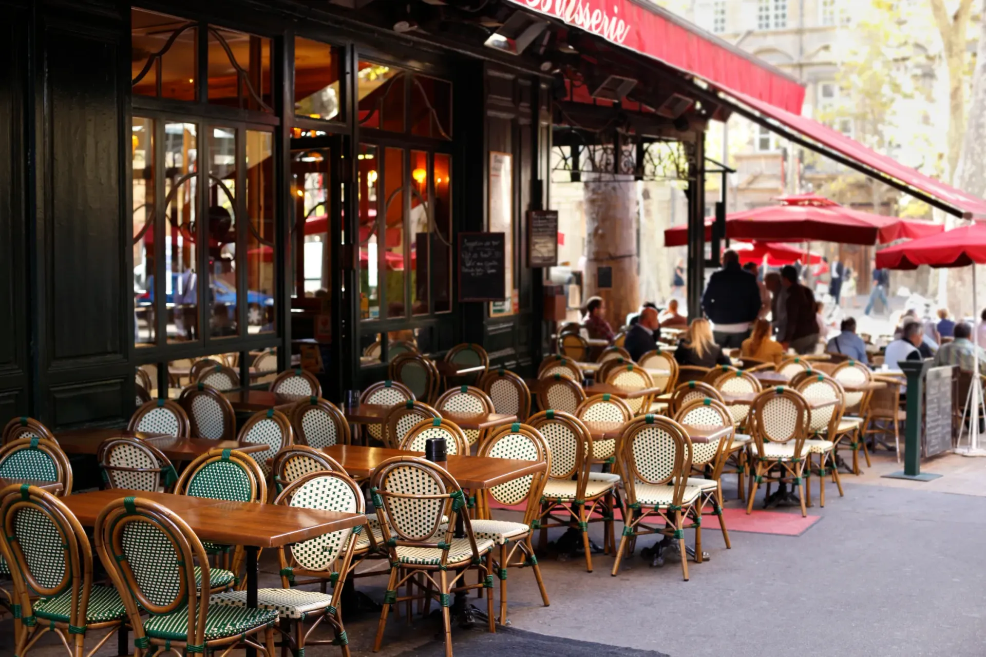 Outdoor seating area of a Parisian-style café with empty wicker chairs and wooden tables under a red awning.