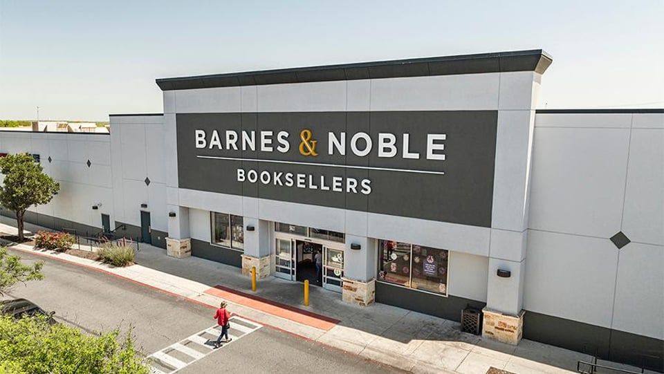 A Barnes & Noble bookstore storefront on a sunny day with a person crossing the street in the foreground.