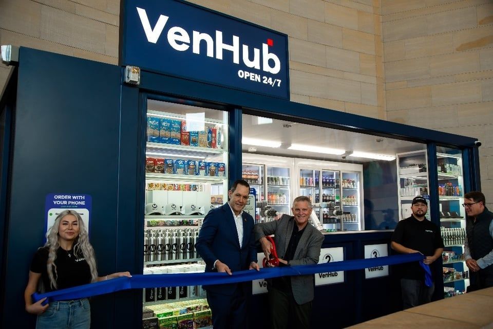 Four people cutting a blue ribbon at the opening of a VenHub, a 24/7 automated retail storefront.