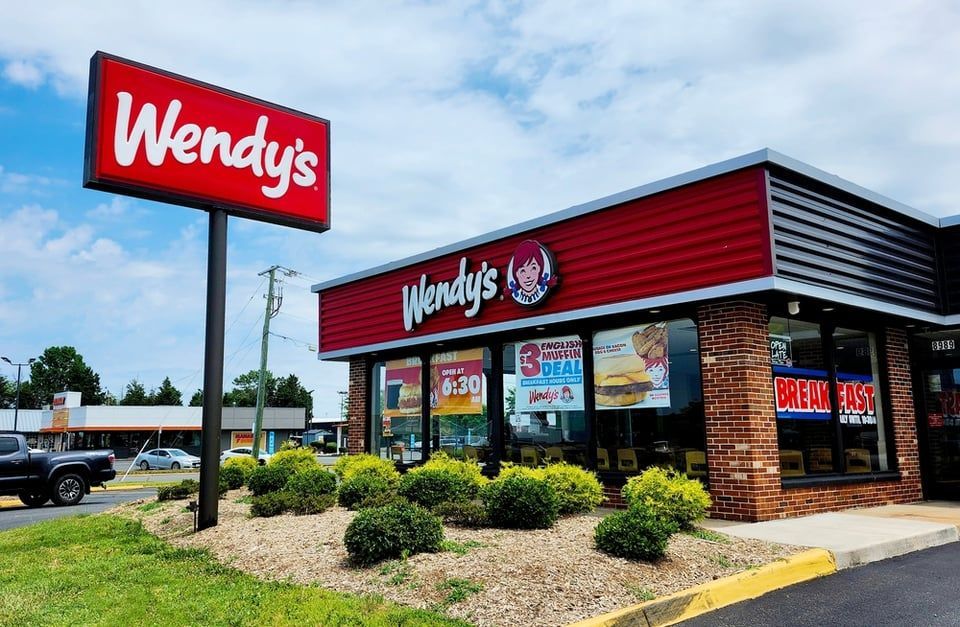A Wendy's restaurant building and its prominent red rectangular sign under a partly cloudy sky.