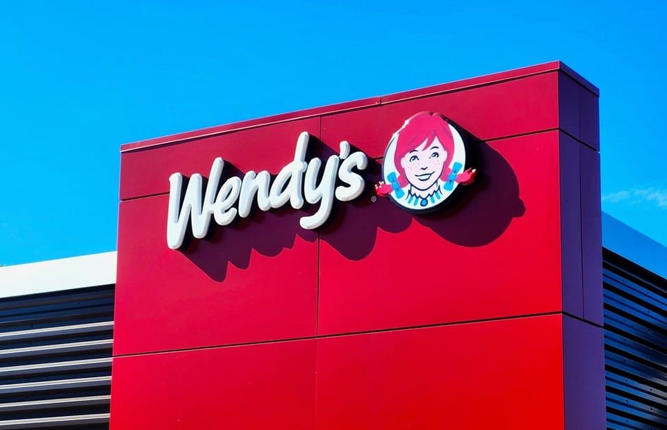 A Wendy's restaurant sign with the white brand logo and the mascot icon against a solid red background under a blue sky.