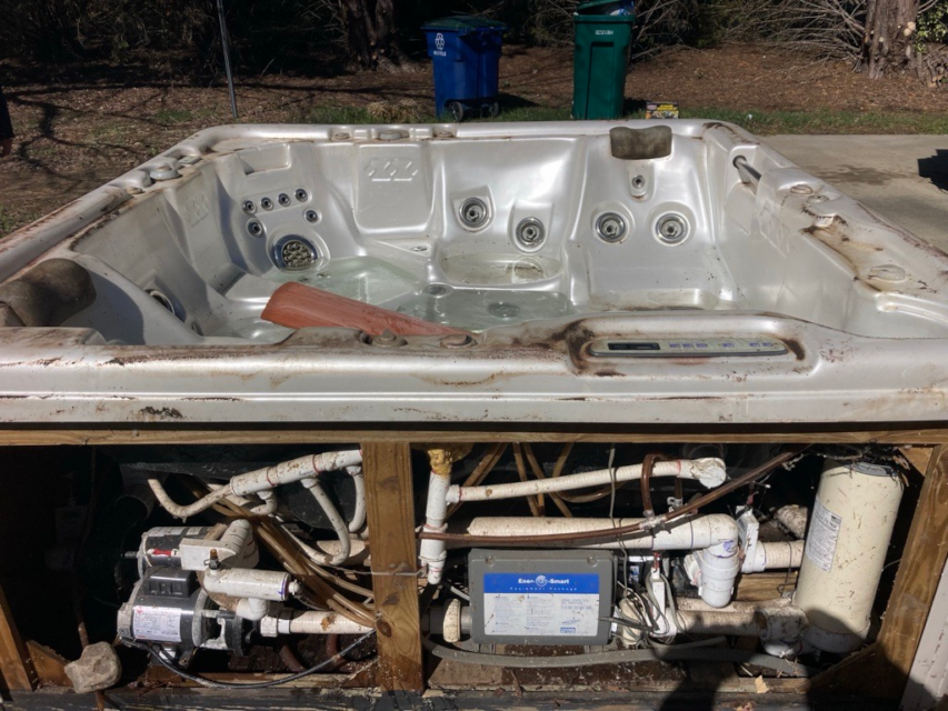A blue dumpster filled with junk is parked on the side of the road.