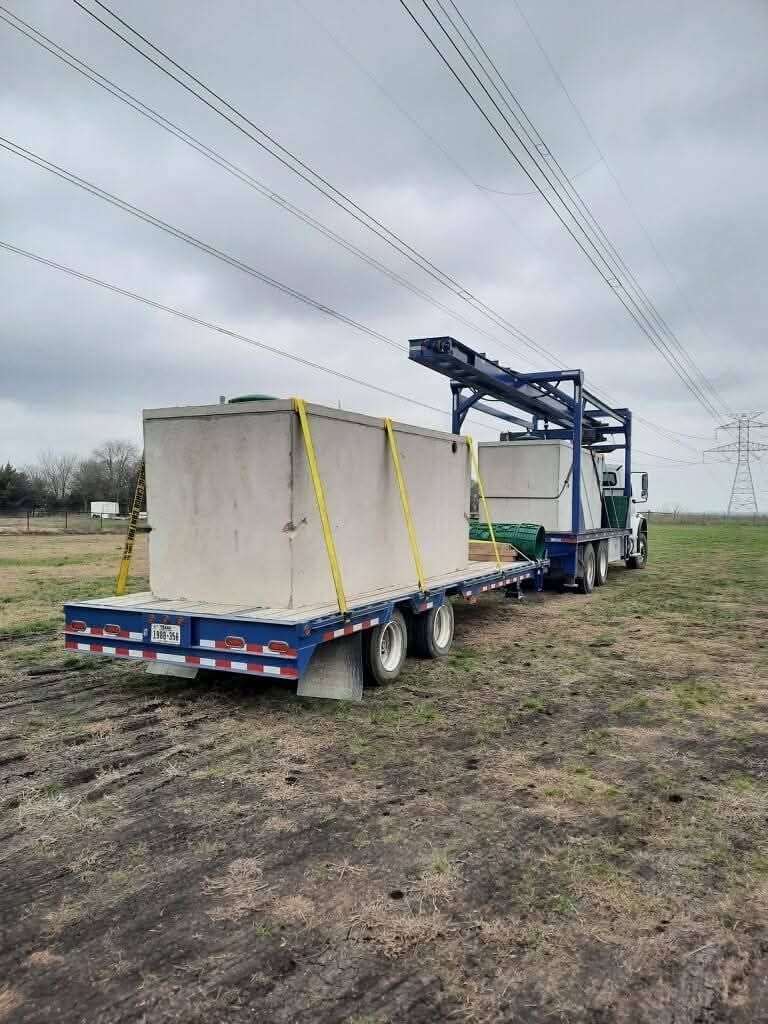 A large concrete container secured on a flatbed truck, being delivered in a rural setting.