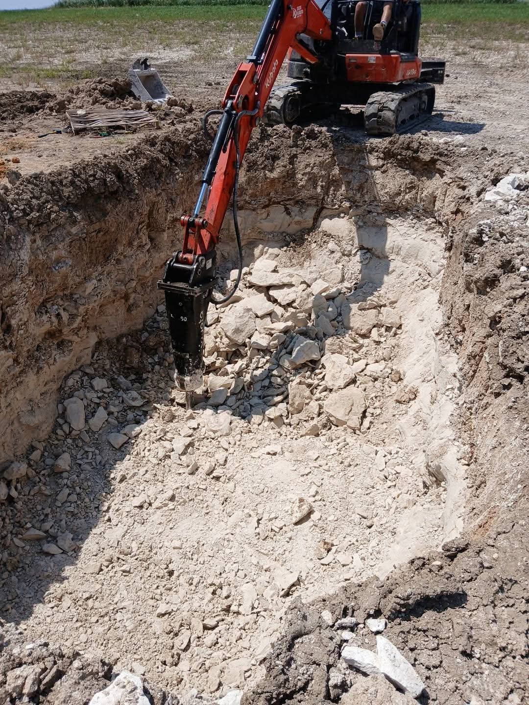 Red excavator breaking up concrete in an excavated area.