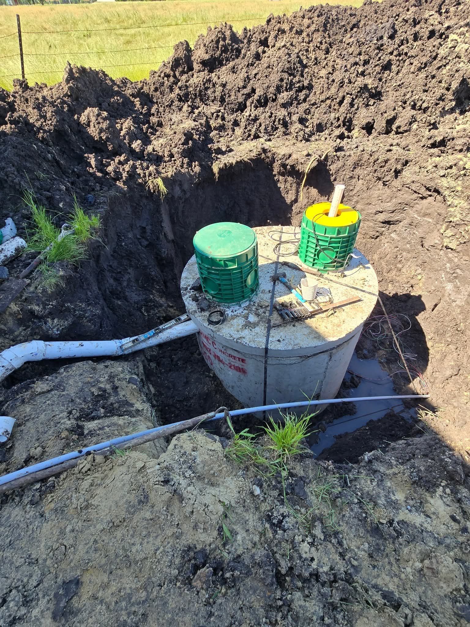 Concrete septic tank with green and yellow covers, in an excavated pit. Pipes lead to it.
