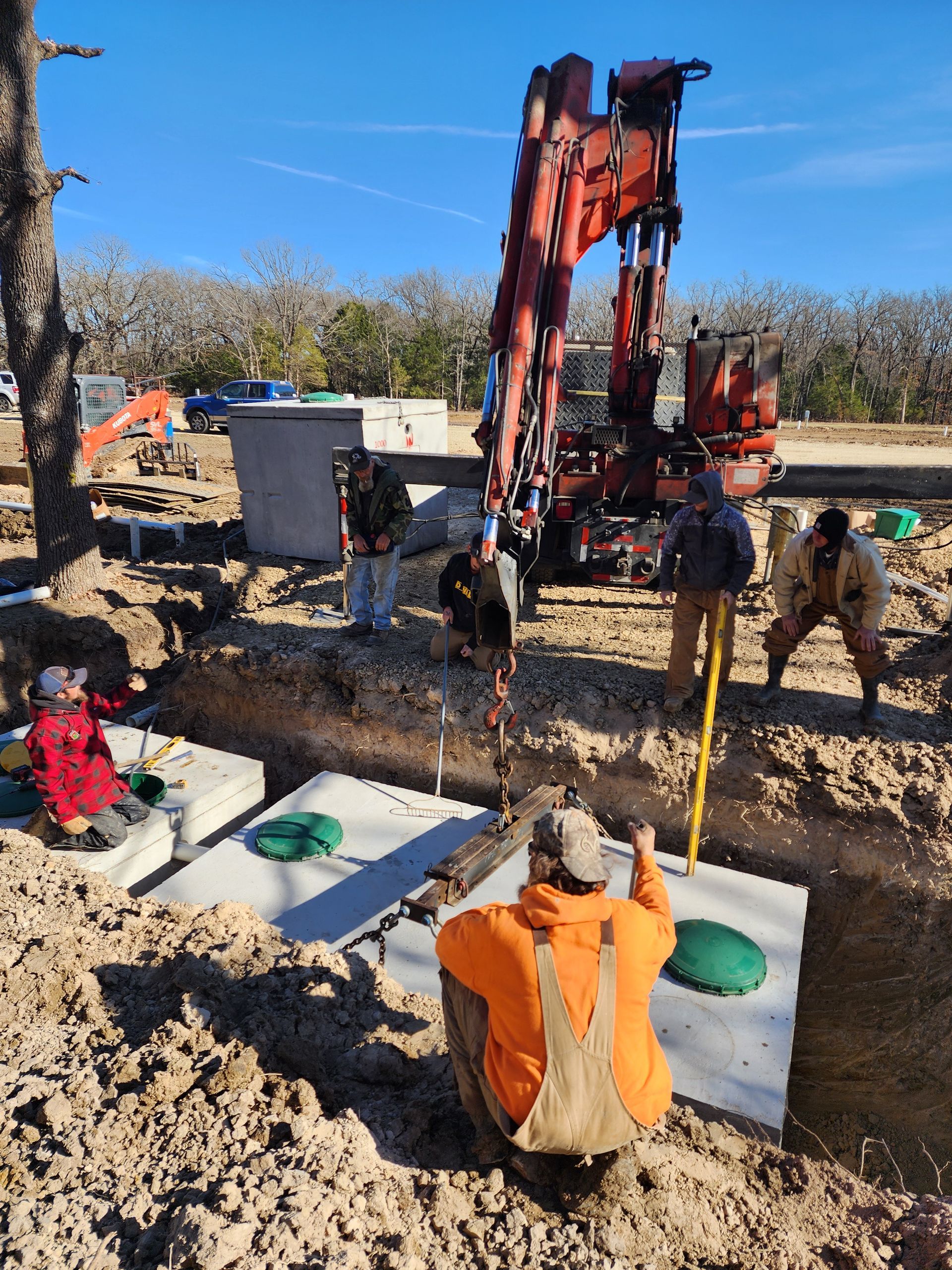 Construction workers installing a septic system. An excavator is in use. Sunny day.