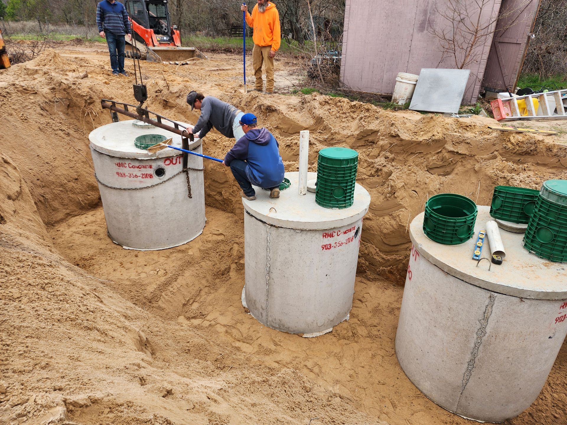 Workers installing concrete septic tanks in a sandy excavation.