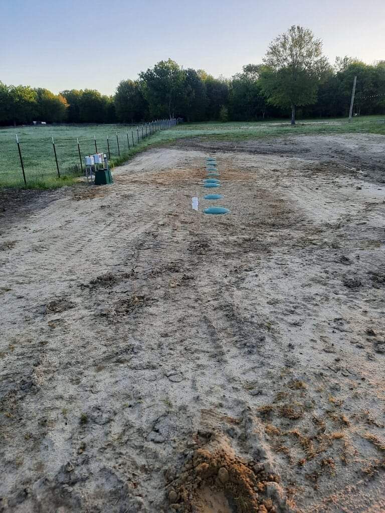 Dirt field with blue objects in a line, trees and fence in the background.