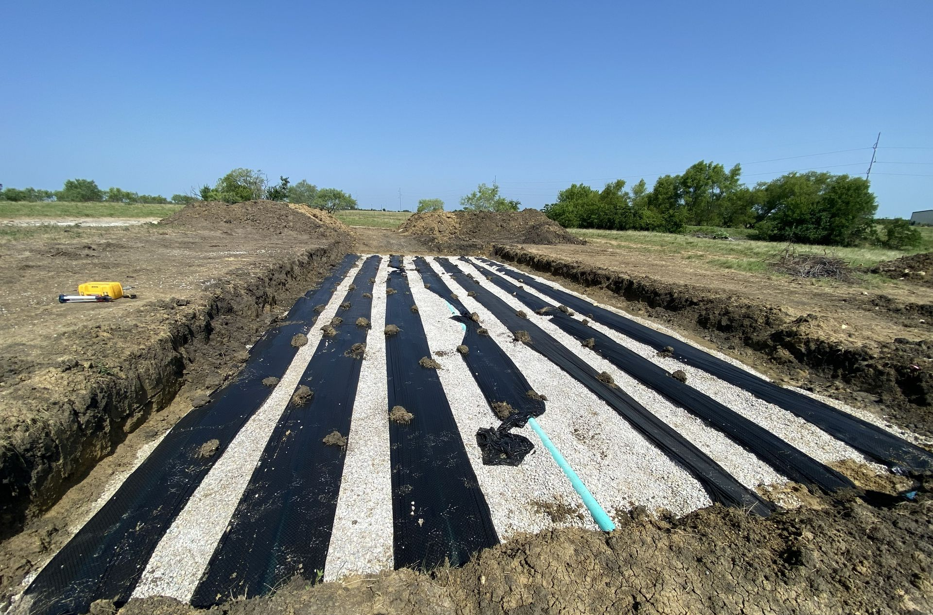 Trenches lined with black fabric and gravel for an underground septic system, outdoors.