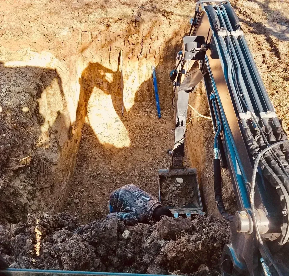 Person working in a deep trench with an excavator. Dirt and brown soil.