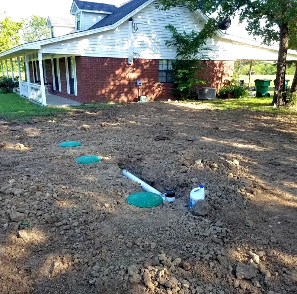 Installation site with a house, exposed pipes, and buried septic tank covers.
