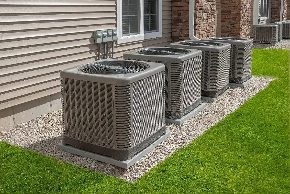 A row of air conditioners are sitting in front of a house.