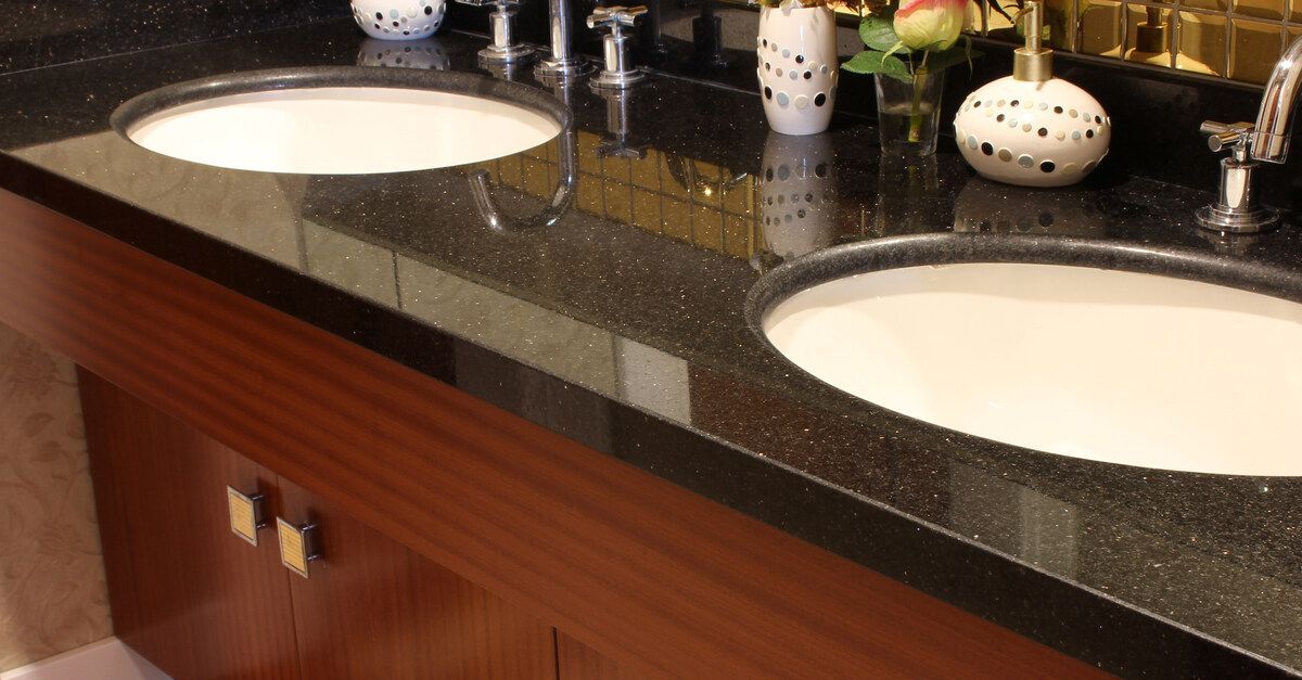 A dark bathroom countertop with two sinks installed in the center. Wood cabinets are at the bottom of the counter.