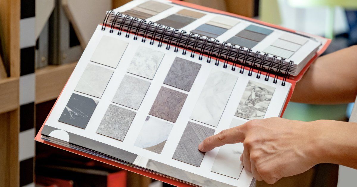 A person is pointing to a stone sample that is inside of a large red book. The book is full of many stone samples.