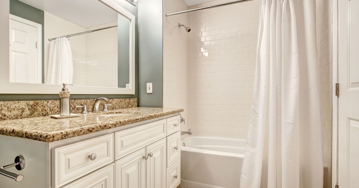 A small bathroom with a vanity that features a granite countertop. The vanity is next to a shower with its curtain open.