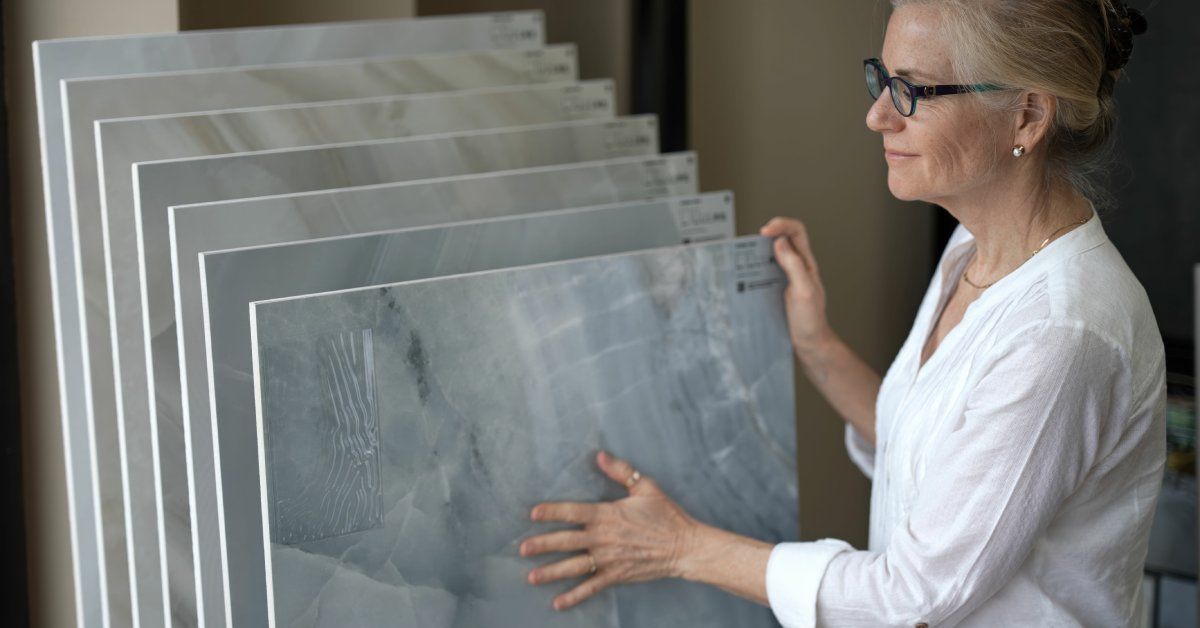 Seven gray stone samples stacked against one another. A person wearing glasses touches the smallest sample.