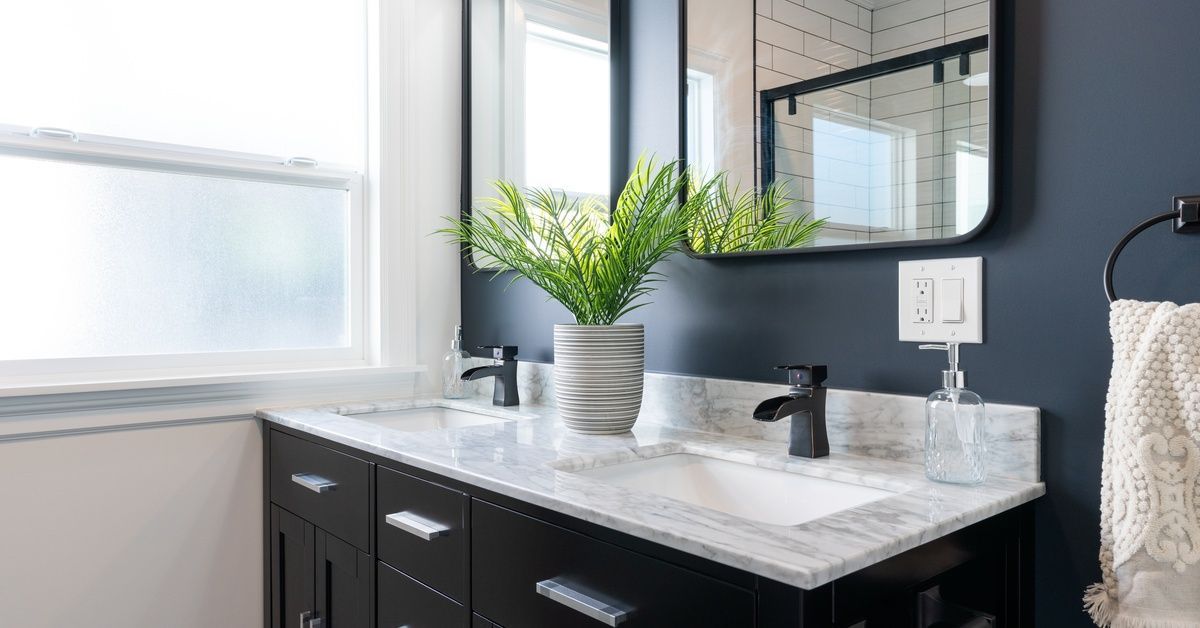 A brightly lit bathroom with a large vanity against the wall. The vanity drawers are black with a stone countertop.