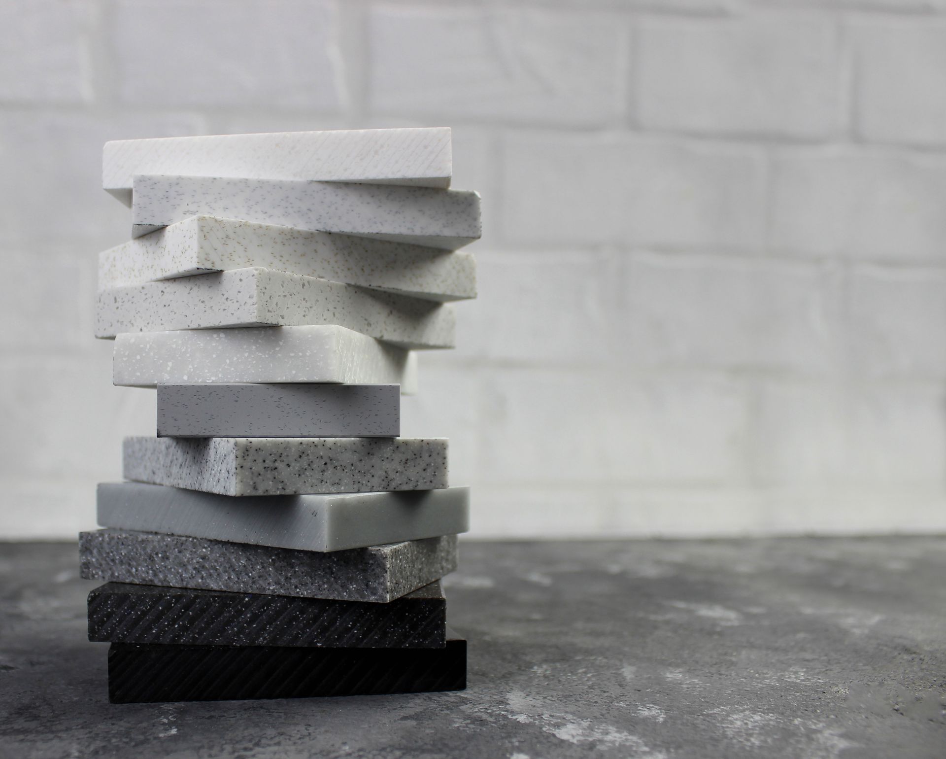 Eleven small stone countertop samples in different shades of gray, white, and black. The samples are