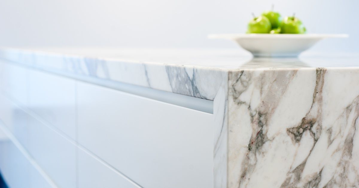 A marble countertop with a mitered edge in a residential kitchen. A plate full of green apples is on