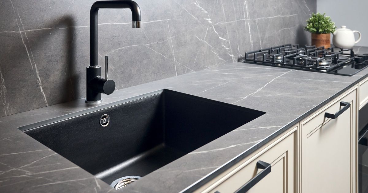 A contemporary kitchen sink area with a matte countertop and a gas burning stove on the far right side.