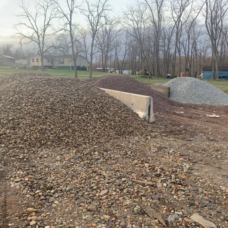 Three piles of construction gravel in varying colors—tan, brown, and grey—separated by concrete barriers in a yard.